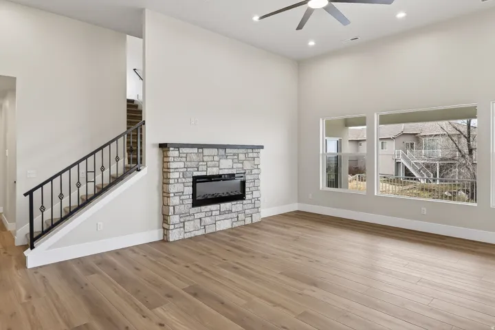 Unfurnished living room featuring a high ceiling, a stone fireplace, light wood-style flooring, a ceiling fan, and recessed lighting