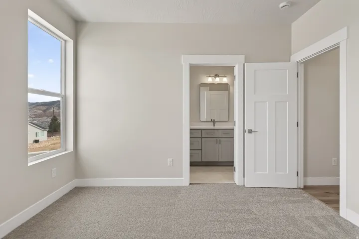 Unfurnished bedroom featuring ensuite bathroom and light colored carpet