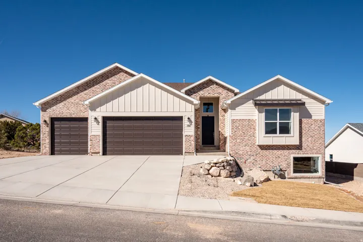 View of front of property with an attached garage, board and batten siding, driveway, and brick siding