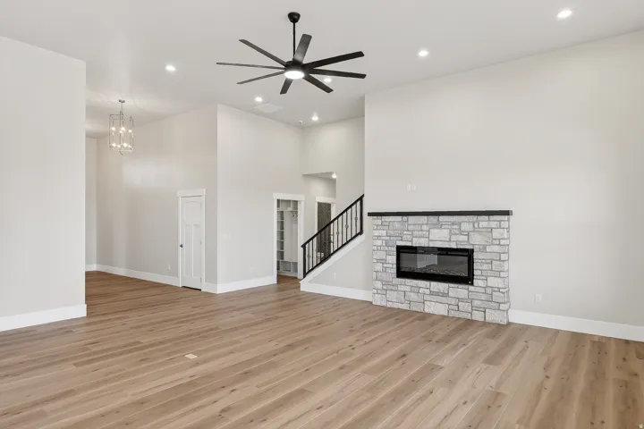 Unfurnished living room with a ceiling fan, a high ceiling, a stone fireplace, light wood-style flooring, and hanging lights