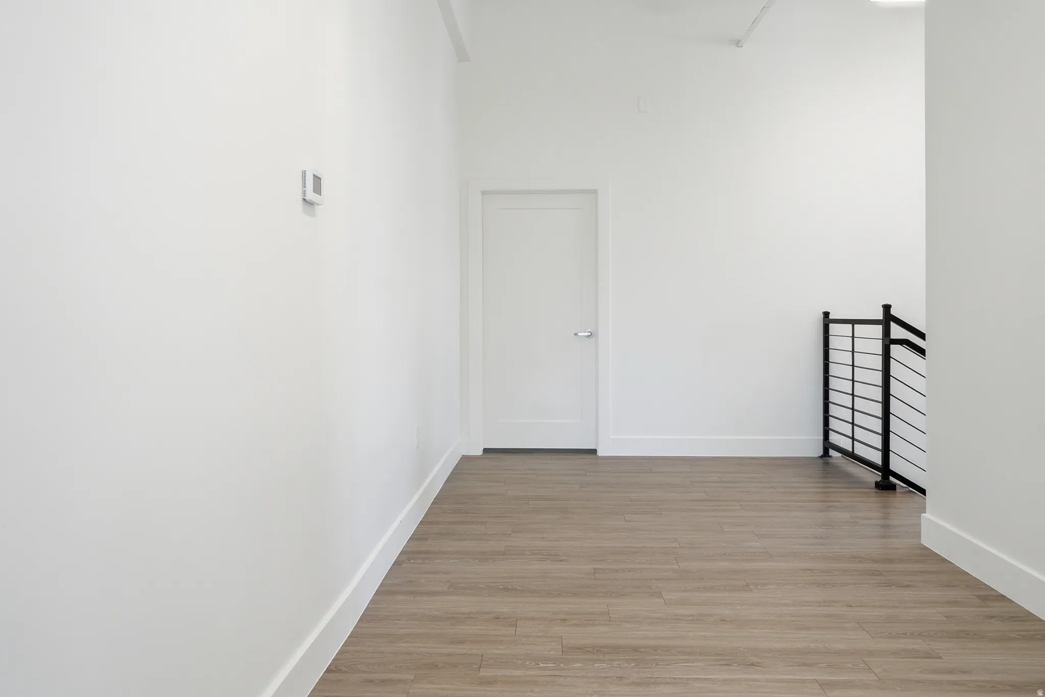Corridor featuring a high ceiling, light wood-style flooring, and an upstairs landing