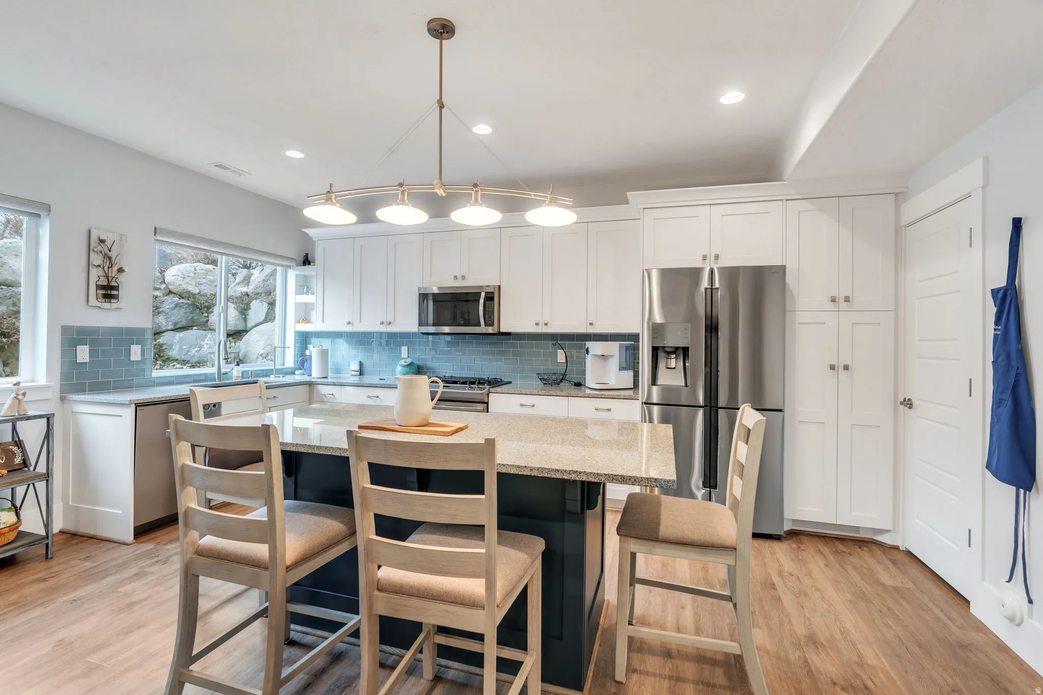 Kitchen featuring stainless steel appliances, white cabinets, light stone countertops, light wood finished floors, and a center island