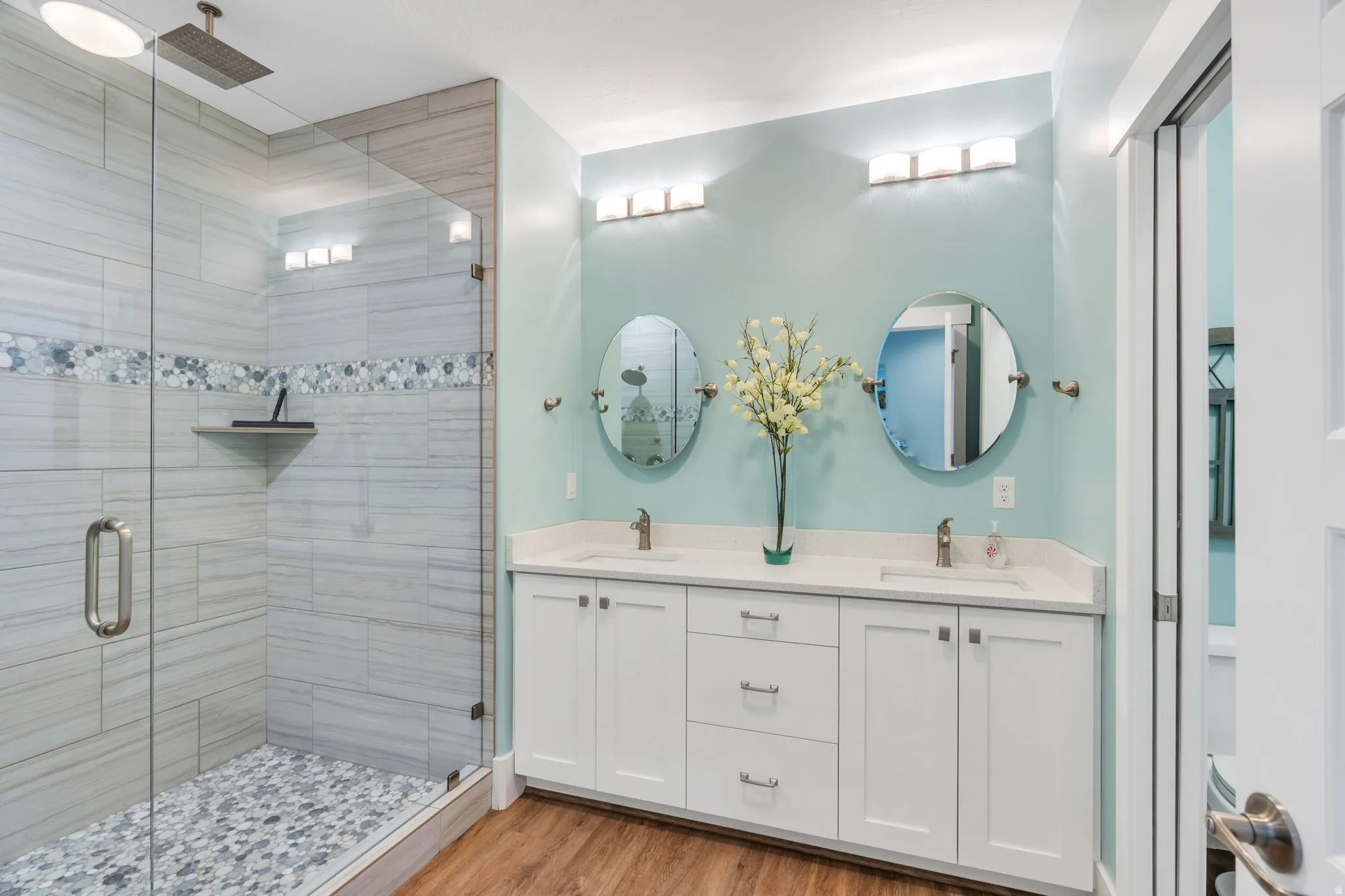 Full bath with double vanity, a shower stall, and light wood finished floors