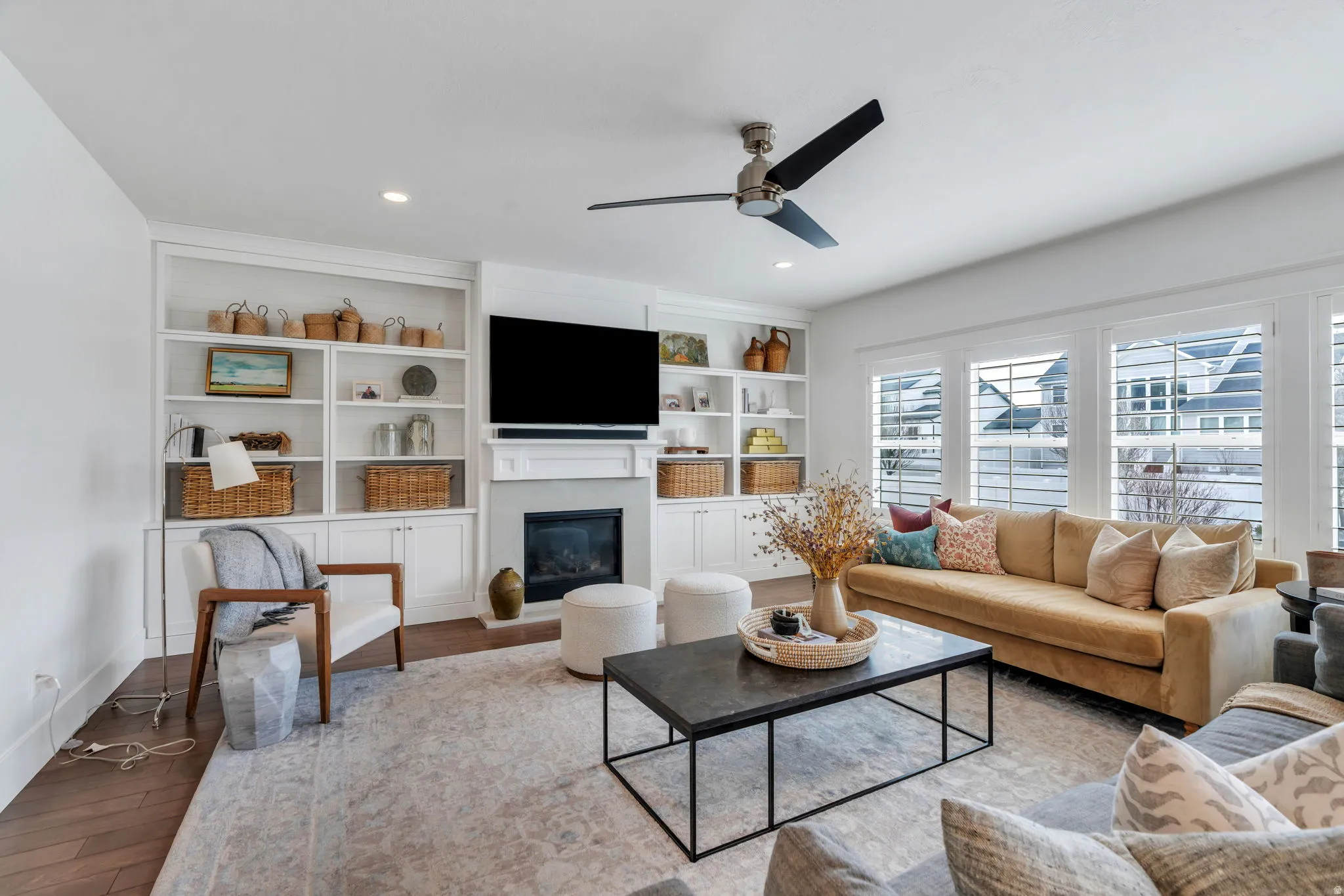 Living room with wood finished floors, a glass covered fireplace, ceiling fan, built in shelves, and recessed lighting