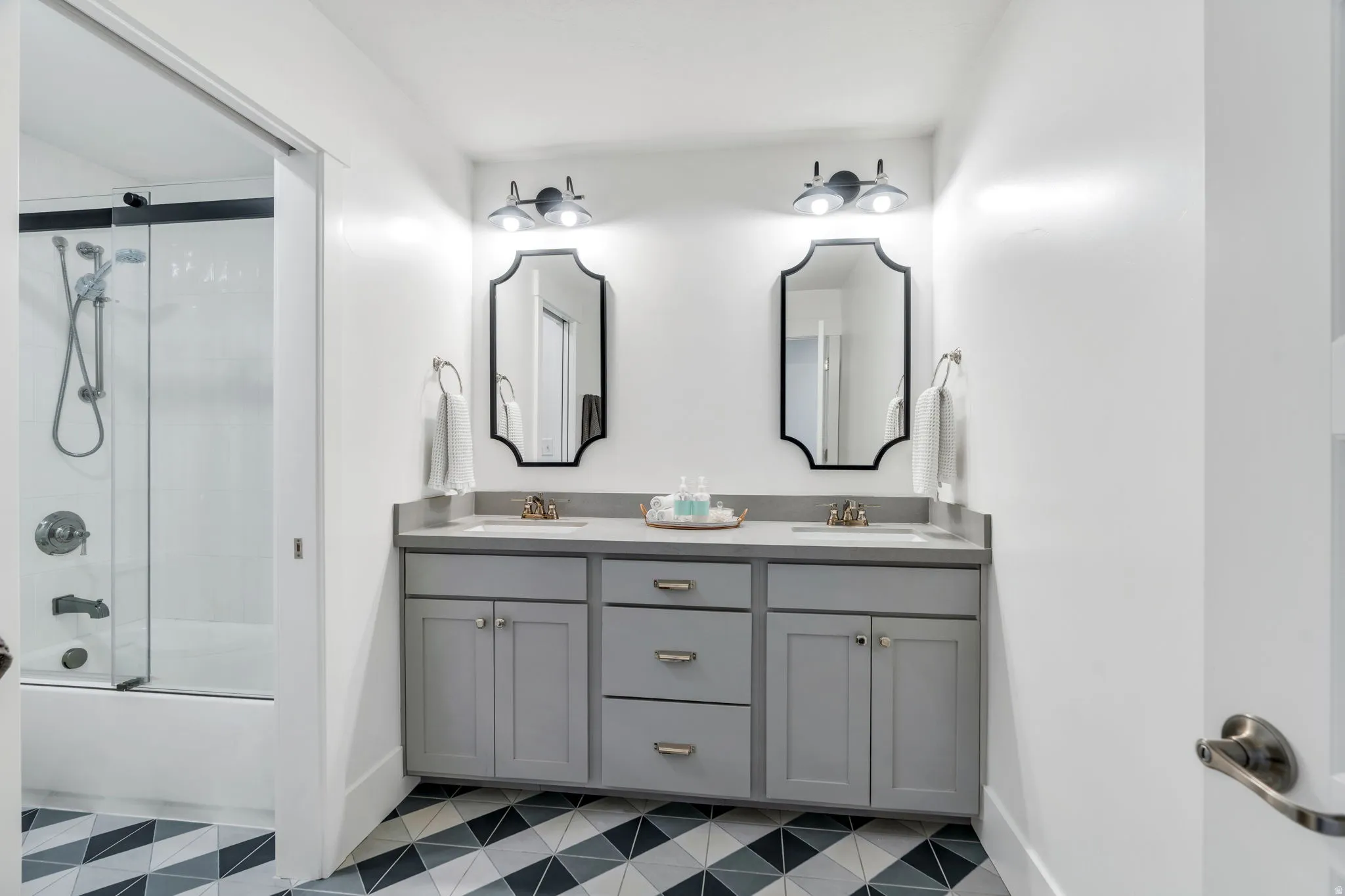 Full bathroom featuring double vanity, light flooring, and enclosed tub / shower combo