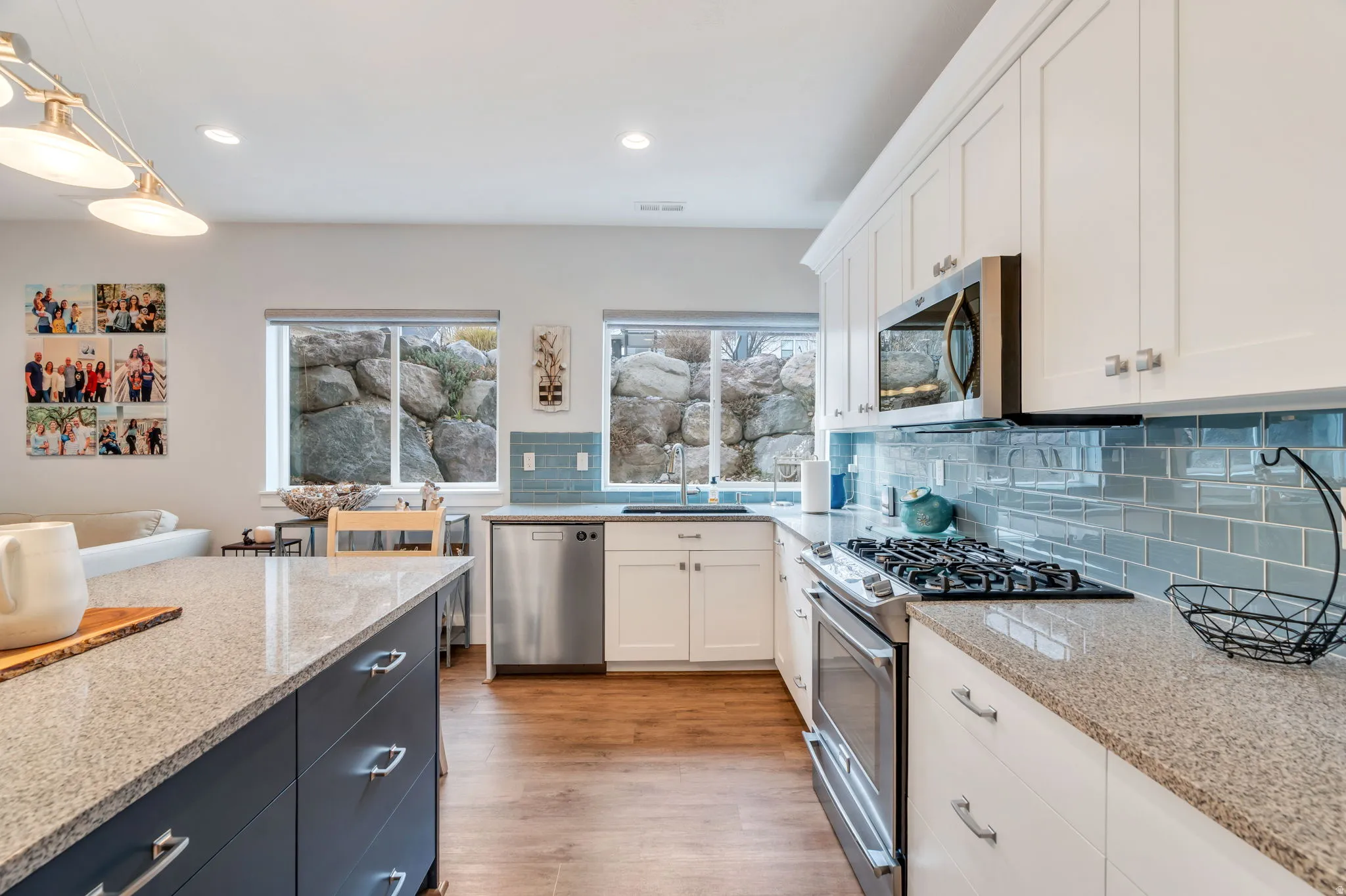 Two tone kitchen with stainless steel appliances, dual tone cabinets, light stone counters, backsplash, and light wood-style flooring