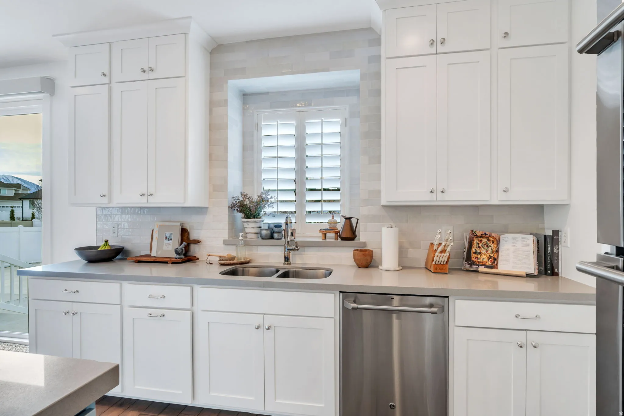 Kitchen featuring white cabinetry, dishwasher, light stone counters, and decorative backsplash