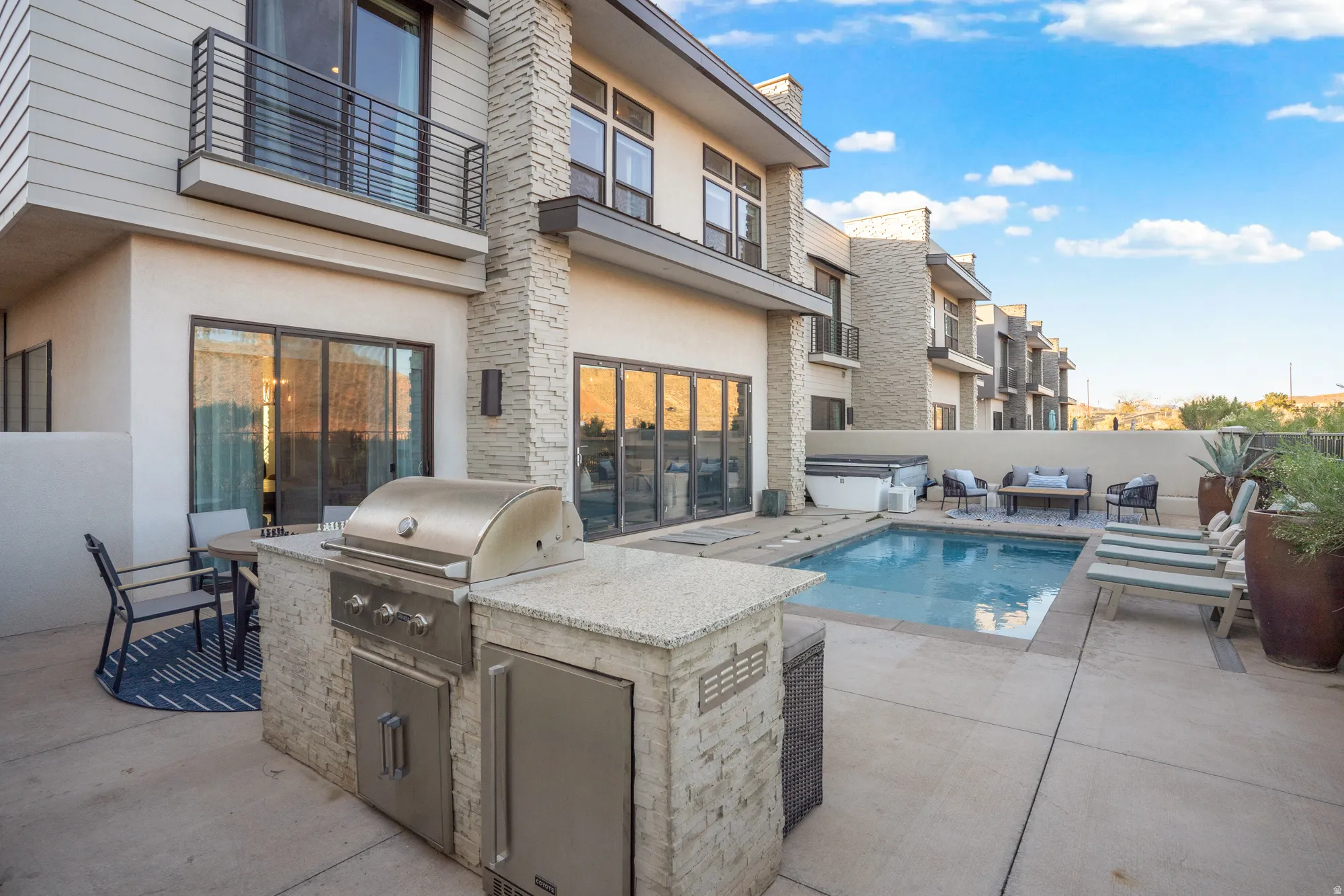 View of pool with an outdoor kitchen with living area, a hot tub, a balcony, and patio surround