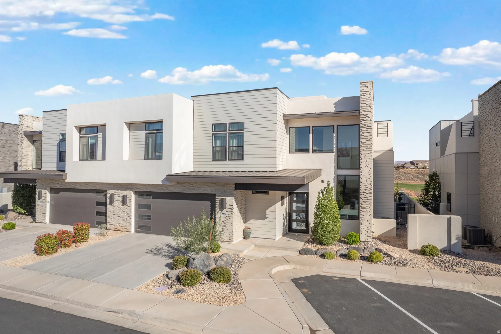 Contemporary home featuring stone siding, stucco siding, a garage, a standing seam roof, and concrete driveway