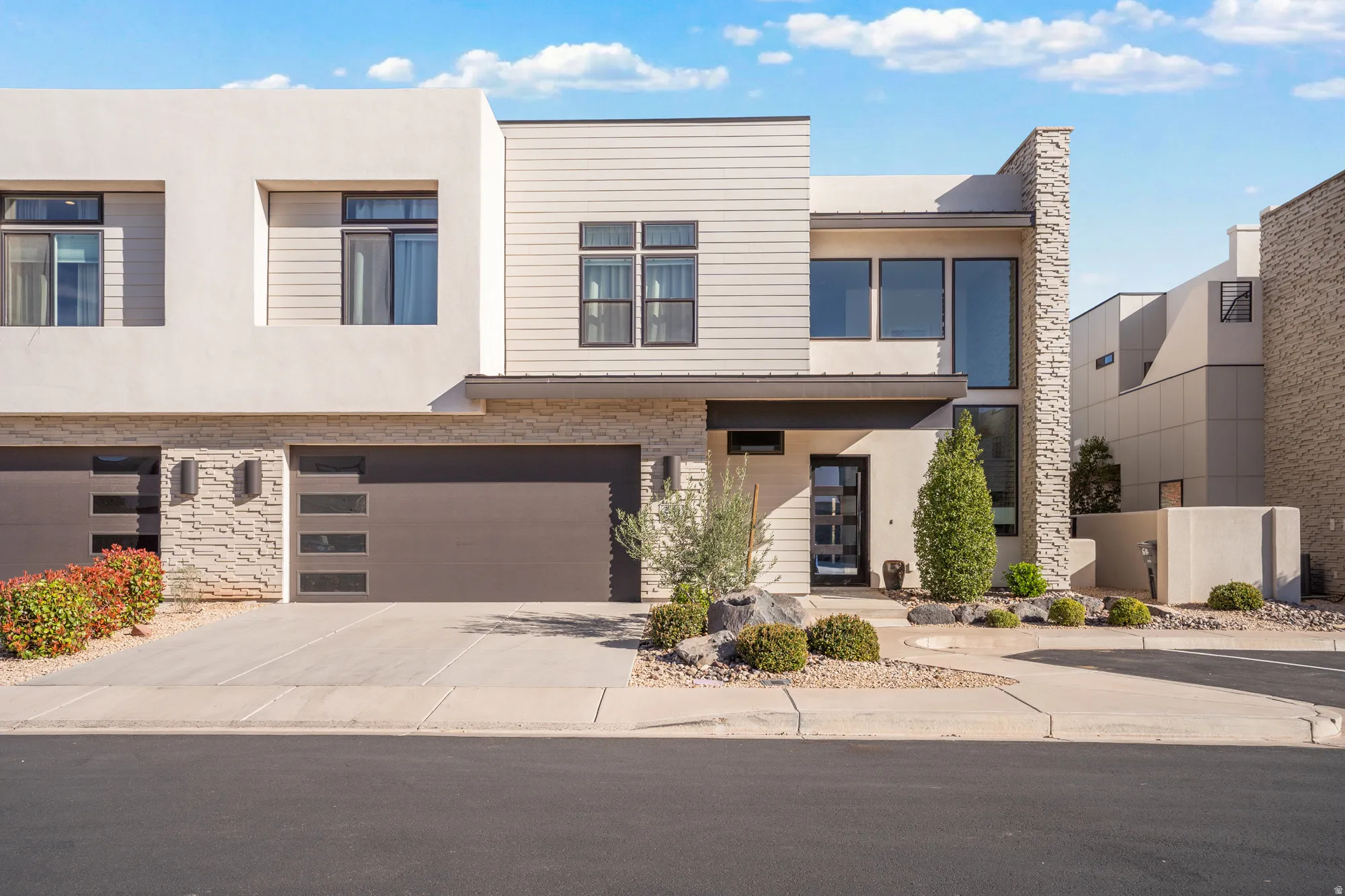 Contemporary house featuring stone siding, stucco siding, a garage, and concrete driveway