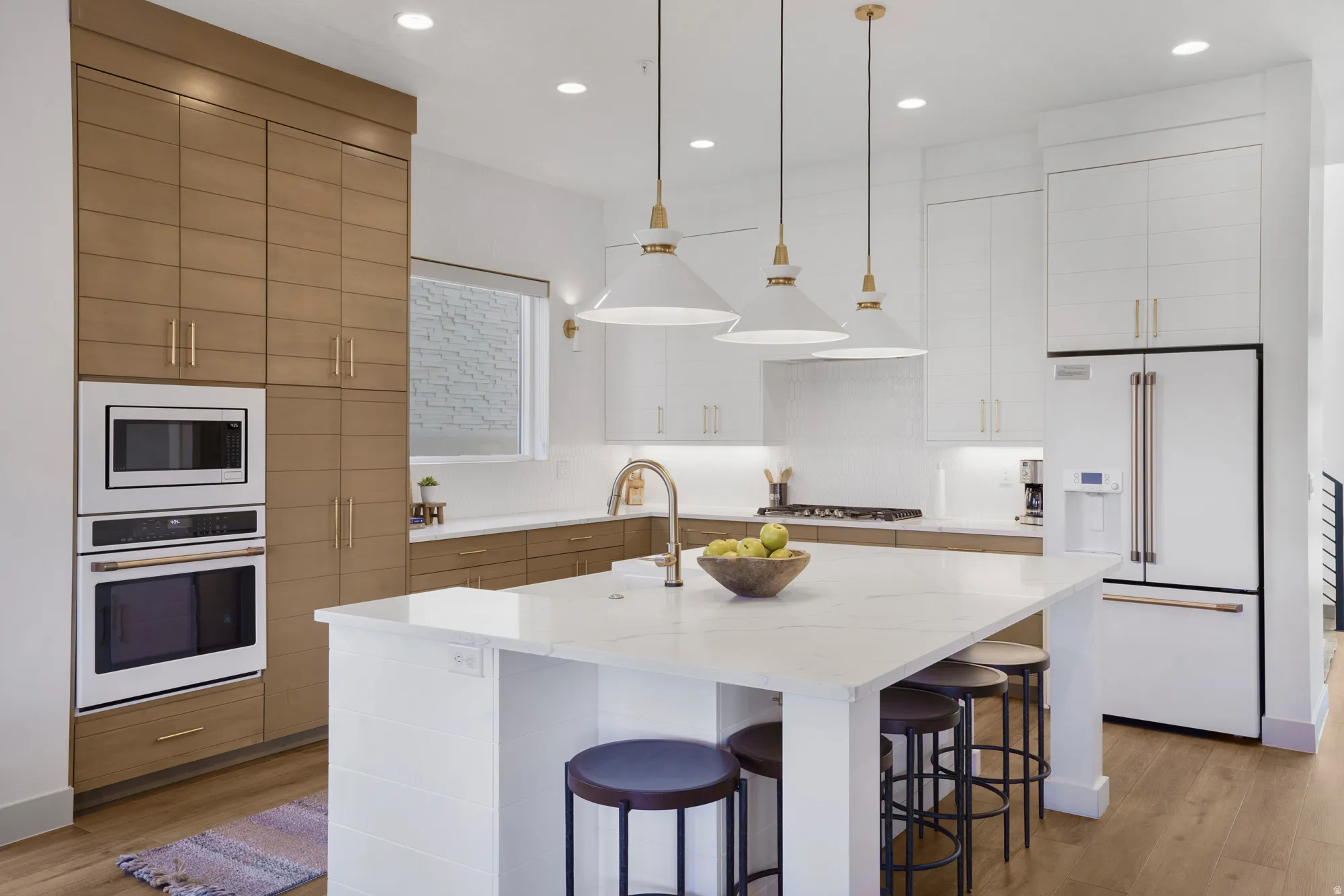 Dual tone kitchen with white appliances, an island with sink, light wood-style flooring, light stone counters, and dual tone cabinetry