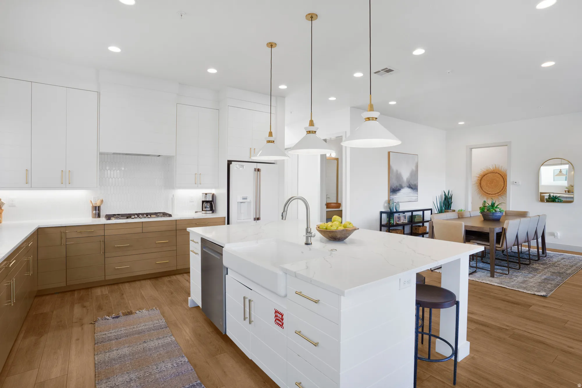 Two tone kitchen featuring two tone color scheme, tasteful backsplash, light wood-type flooring, light stone counters, and decorative light fixtures