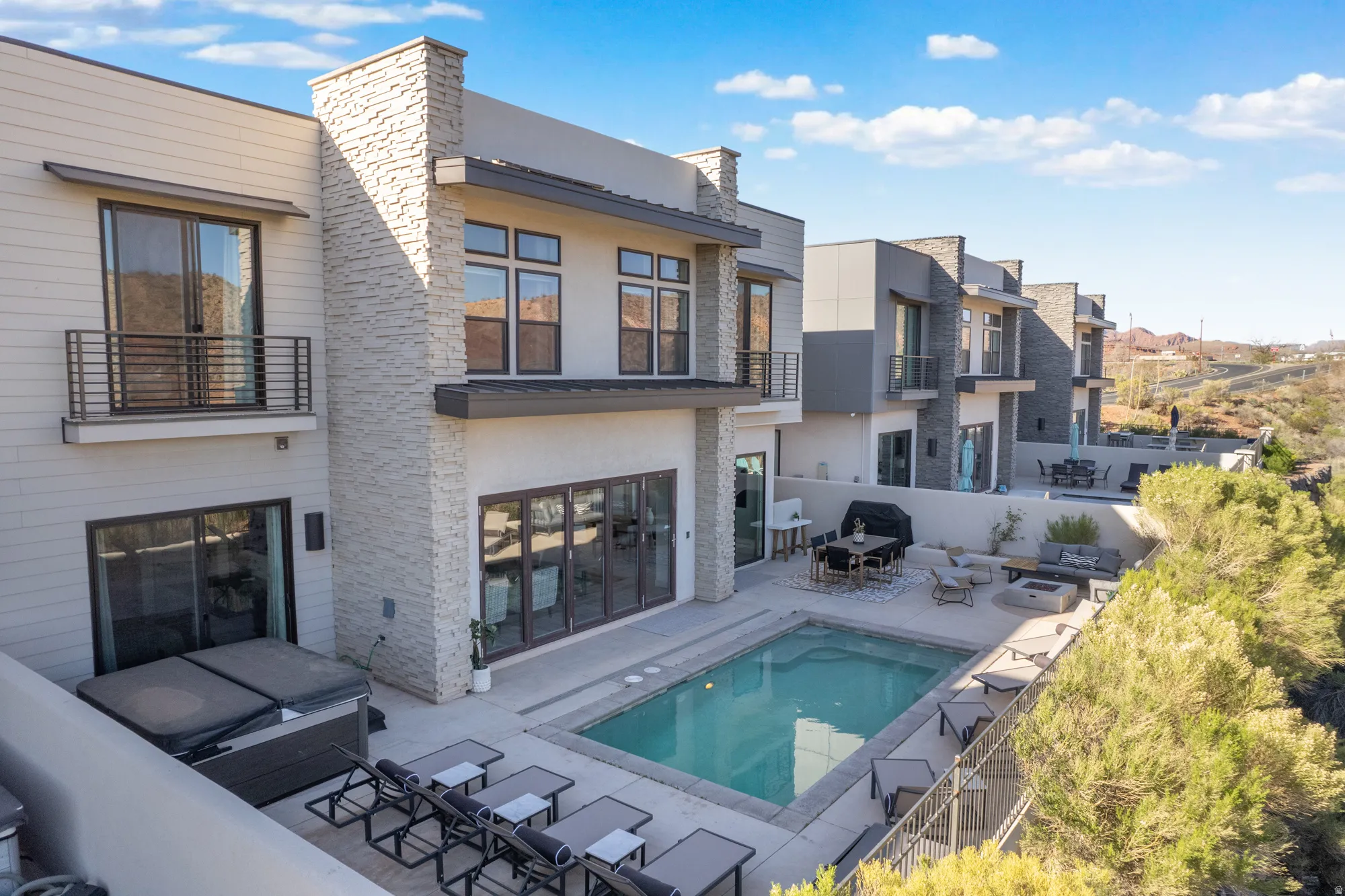 Rear view of property featuring stucco siding, a patio area, a balcony, an outdoor hot tub, and outdoor dining space