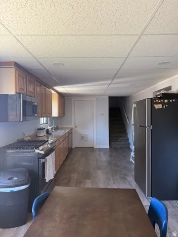 Kitchen featuring stainless steel appliances, a drop ceiling, wood finish cabinets, light countertops, and light wood-type flooring