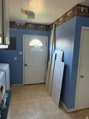 Laundry room featuring light floors, electric panel, a textured ceiling, and washing machine and clothes dryer