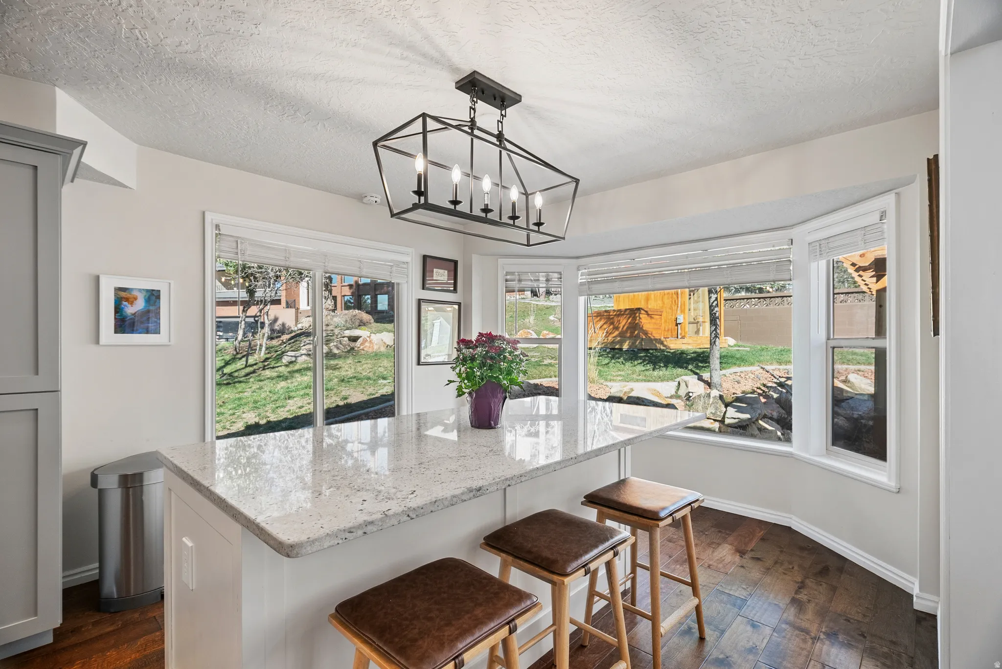 Kitchen with light stone countertops, a kitchen island, dark wood finished floors, a kitchen bar, and a textured ceiling