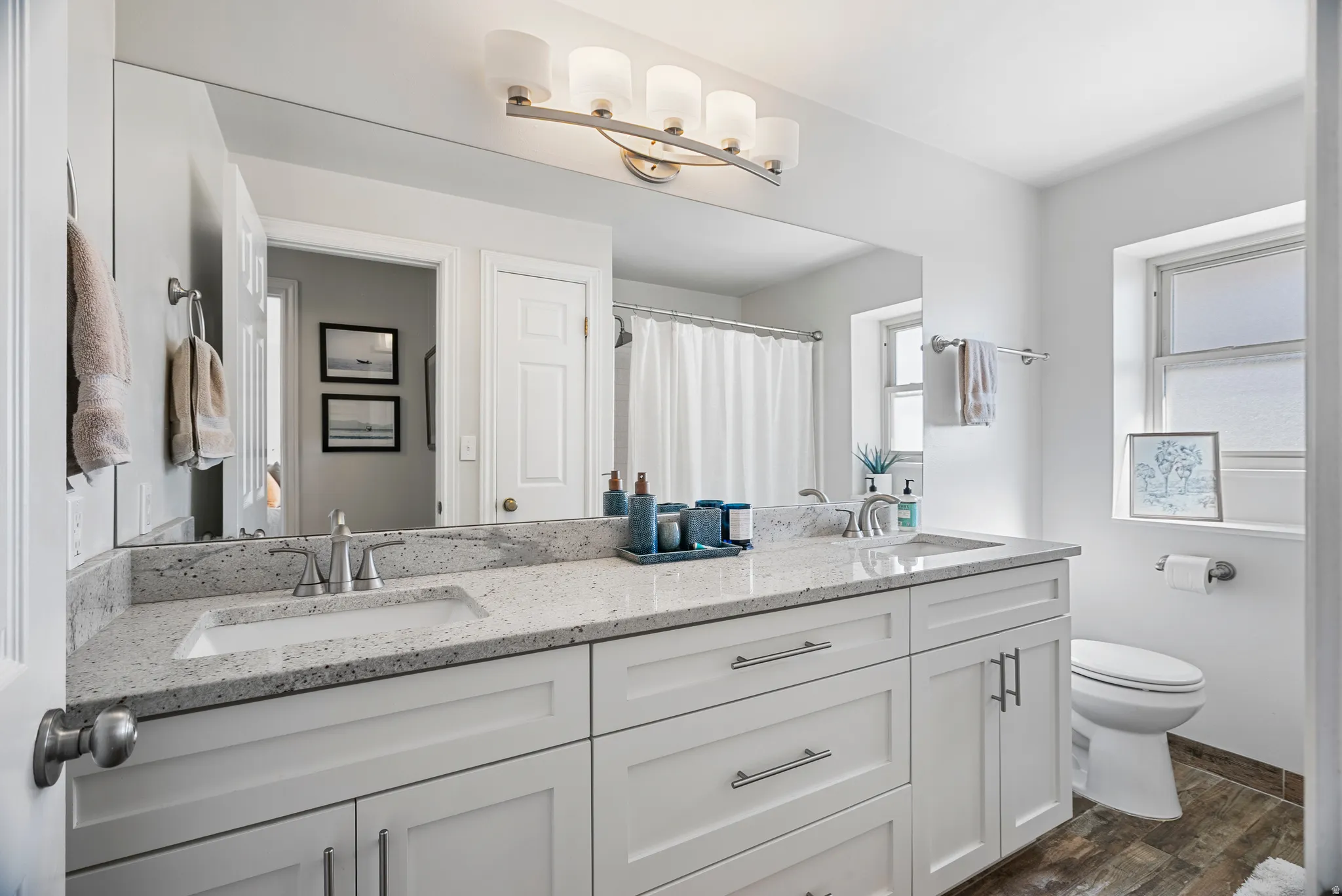 Full bathroom with double vanity, dark wood-style floors, and curtained shower
