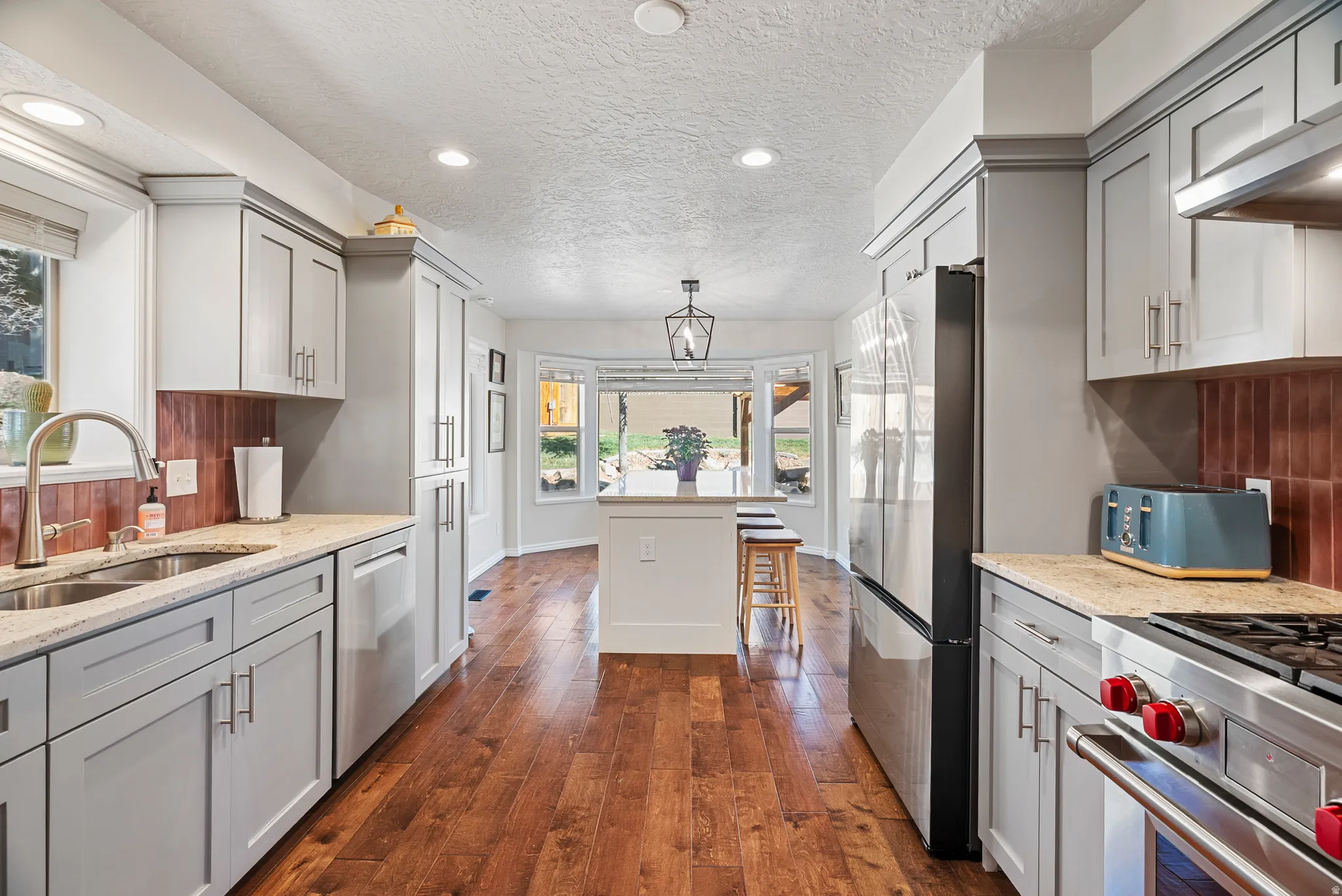 Kitchen with light stone countertops, dark wood-style floors, gray cabinets, stainless steel appliances, and tasteful backsplash