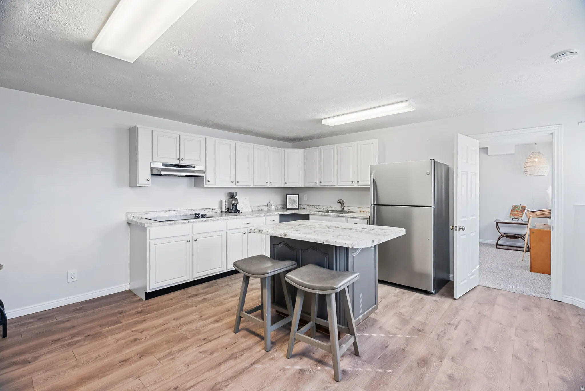 Downstairs: two tone kitchen with freestanding refrigerator, a breakfast bar, a kitchen island, light wood-style flooring, and dual tone cabinetry