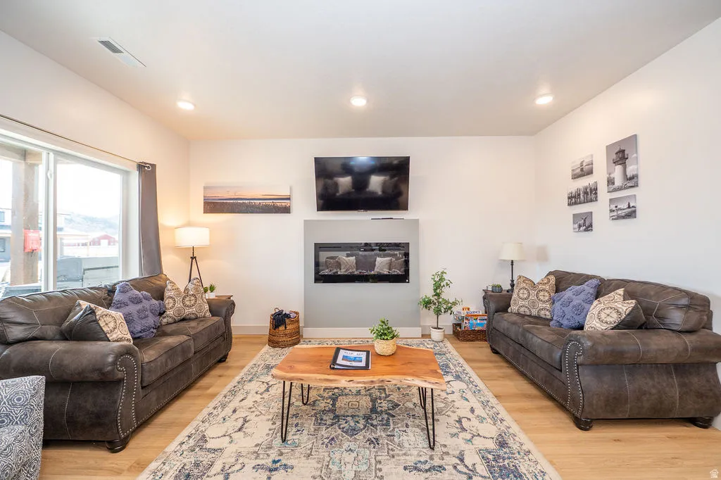 Living room featuring light wood-type flooring, a glass covered fireplace, and recessed lighting