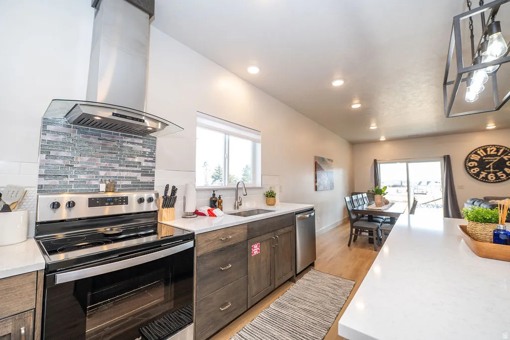 Kitchen featuring stainless steel appliances, island exhaust hood, decorative backsplash, light wood-style flooring, and light stone countertops