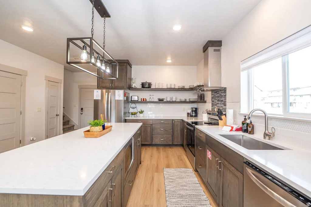 Kitchen featuring stainless steel appliances, pendant lighting, light wood-style flooring, a center island, and light stone countertops