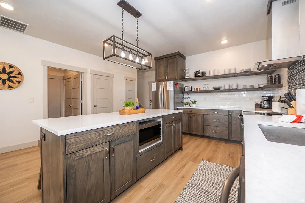 Kitchen featuring decorative backsplash, extractor fan, stainless steel appliances, dark wood finish cabinetry, and a center island