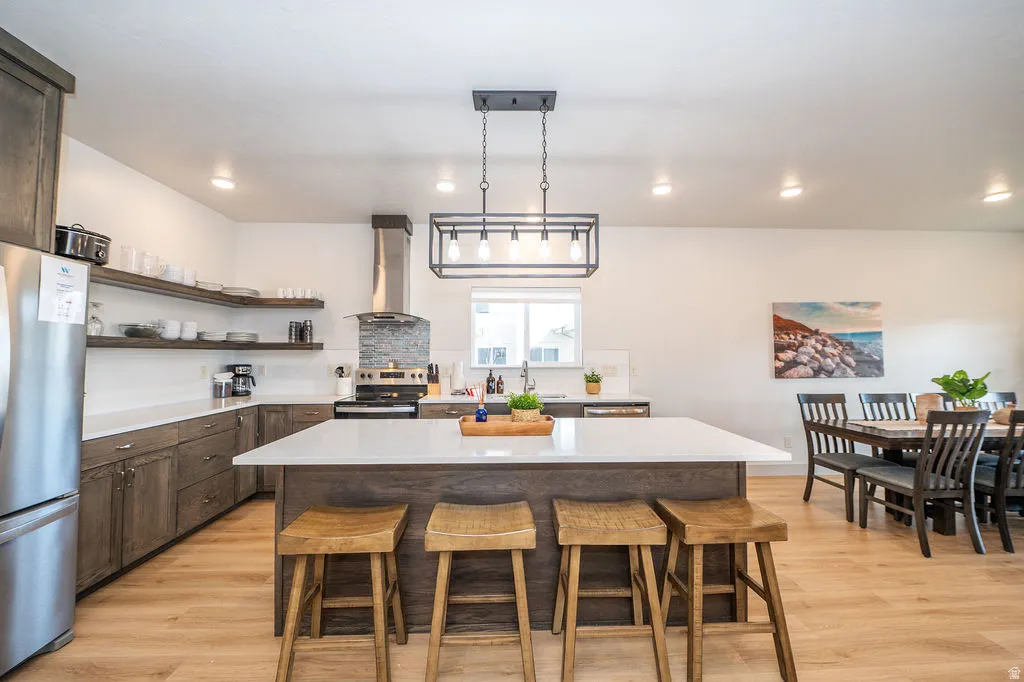 Kitchen with dark wood finish cabinets, stainless steel appliances, a kitchen breakfast bar, open shelves, and light wood-style floors