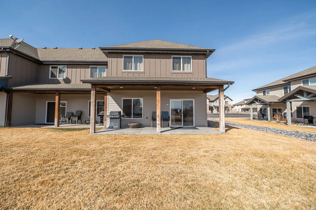 Back of property with a patio, a lawn, a shingled roof, and board and batten siding