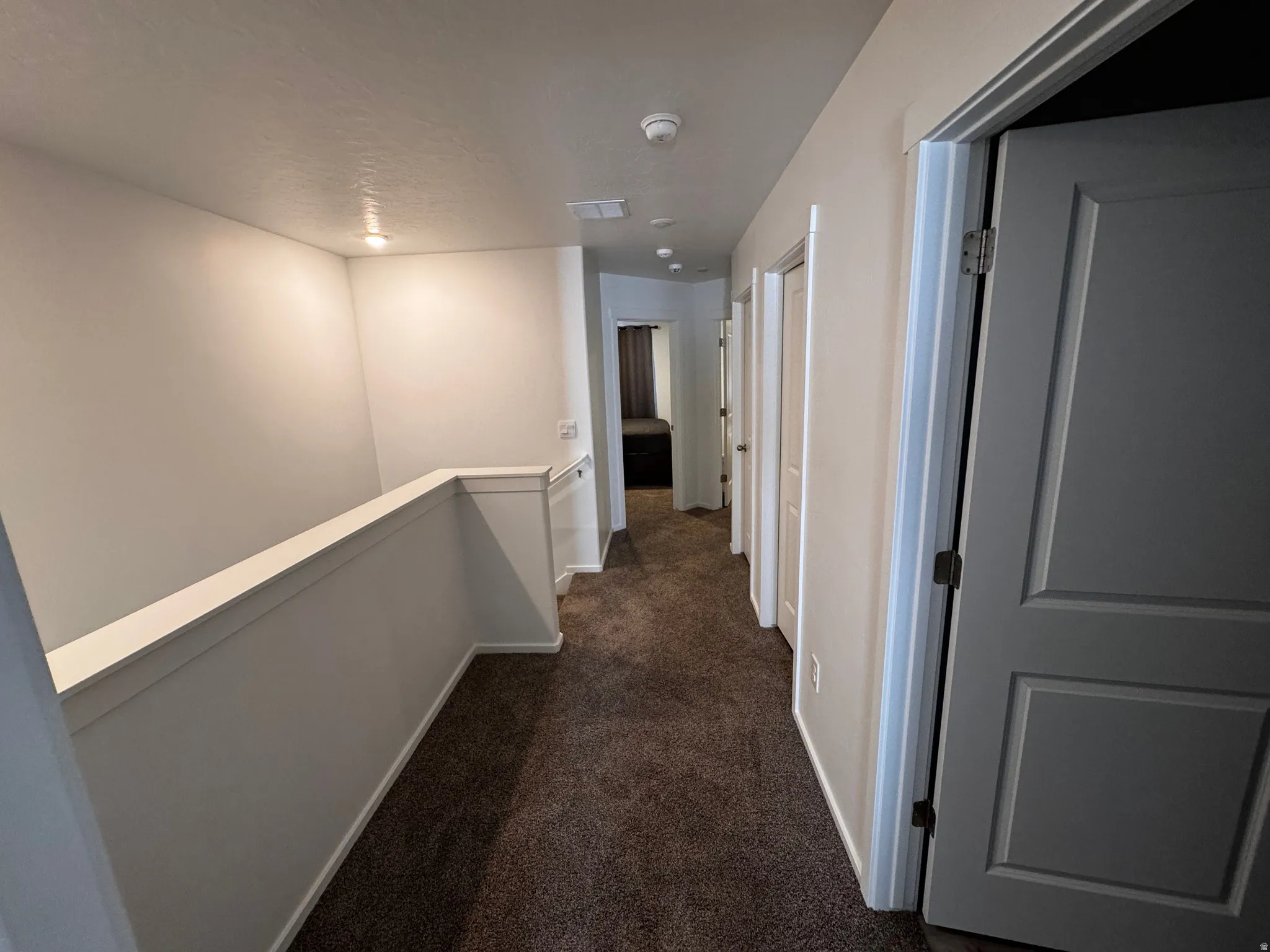 Hallway with dark carpet and an upstairs landing