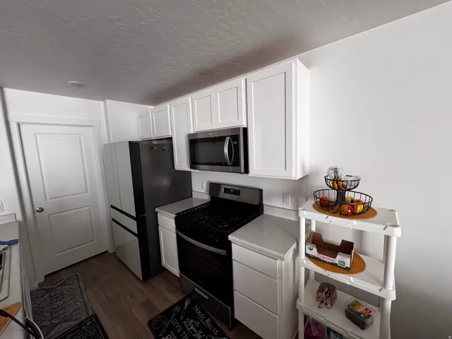 Kitchen with stainless steel appliances, white cabinets, light countertops, dark wood-style floors, and a textured ceiling