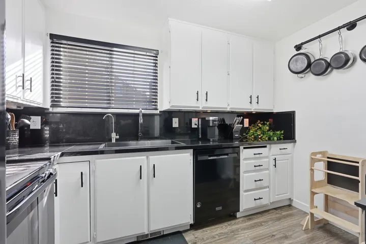 Kitchen featuring dark countertops, white cabinets, dishwasher, light floors, and electric range