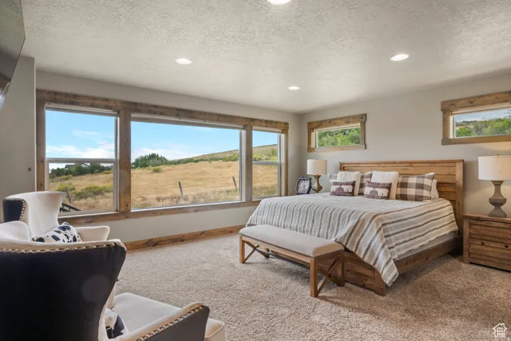 Carpeted bedroom featuring recessed lighting, a textured ceiling, and multiple windows