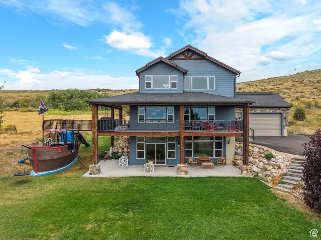 Rear view of house with a patio, a balcony, a lawn, and stone siding