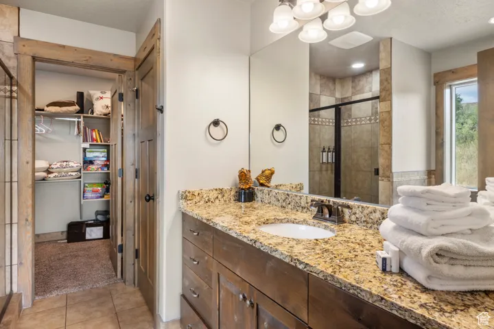 Bathroom featuring vanity, a spacious closet, a shower stall, light tile patterned floors, and a textured ceiling