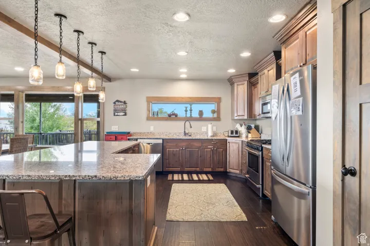Kitchen featuring stainless steel appliances, a textured ceiling, light stone counters, beam ceiling, and dark wood-type flooring