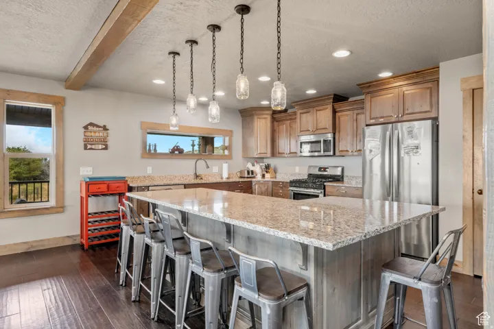 Kitchen with stainless steel appliances, a textured ceiling, dark wood-type flooring, light stone countertops, and a breakfast bar