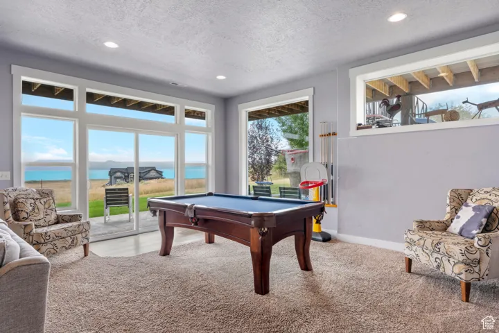 Recreation room featuring a water view, billiards table, light colored carpet, a textured ceiling, and recessed lighting