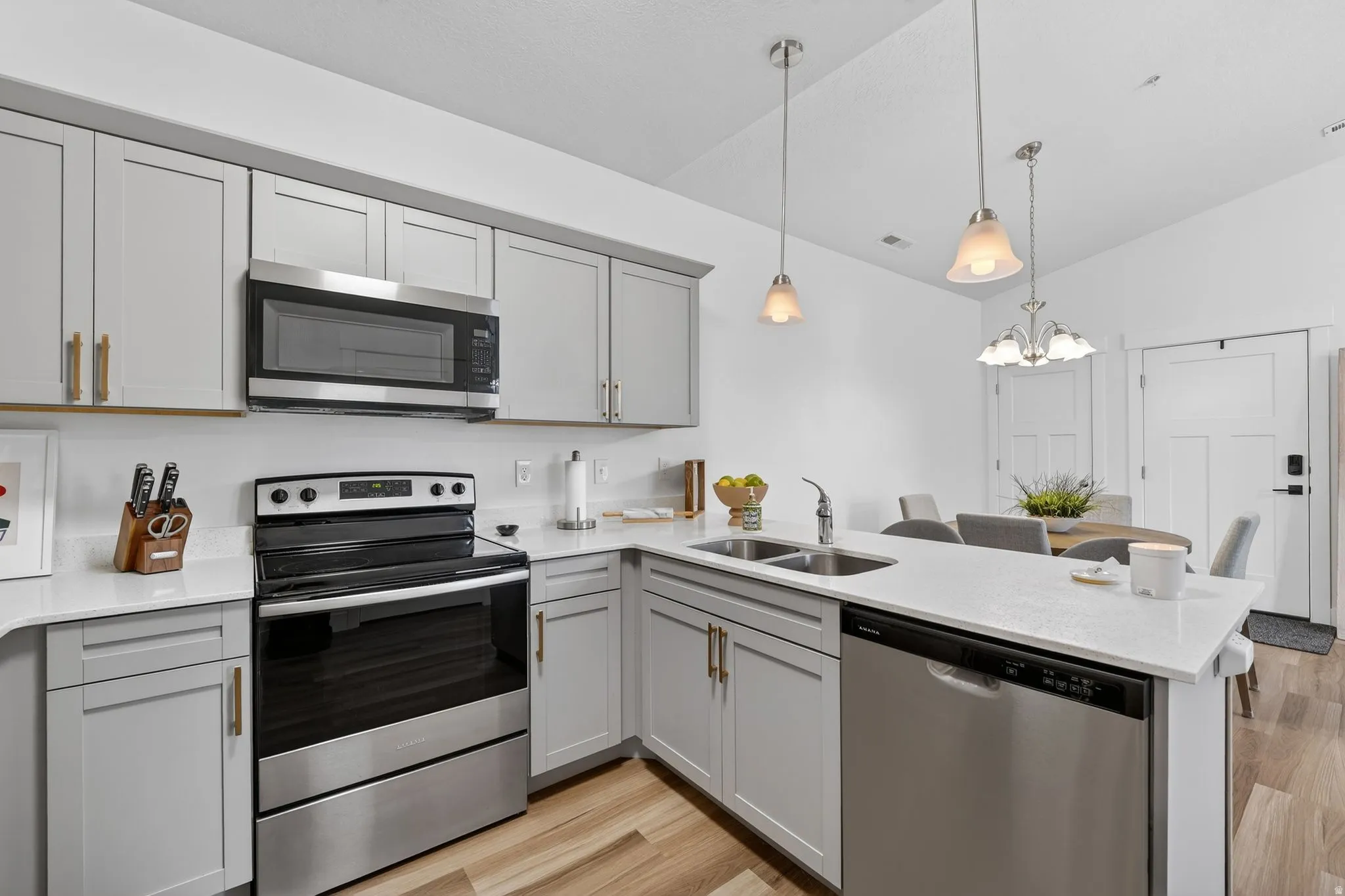 Kitchen featuring stainless steel appliances, a peninsula, light wood-style flooring, gray cabinets, and light stone countertops