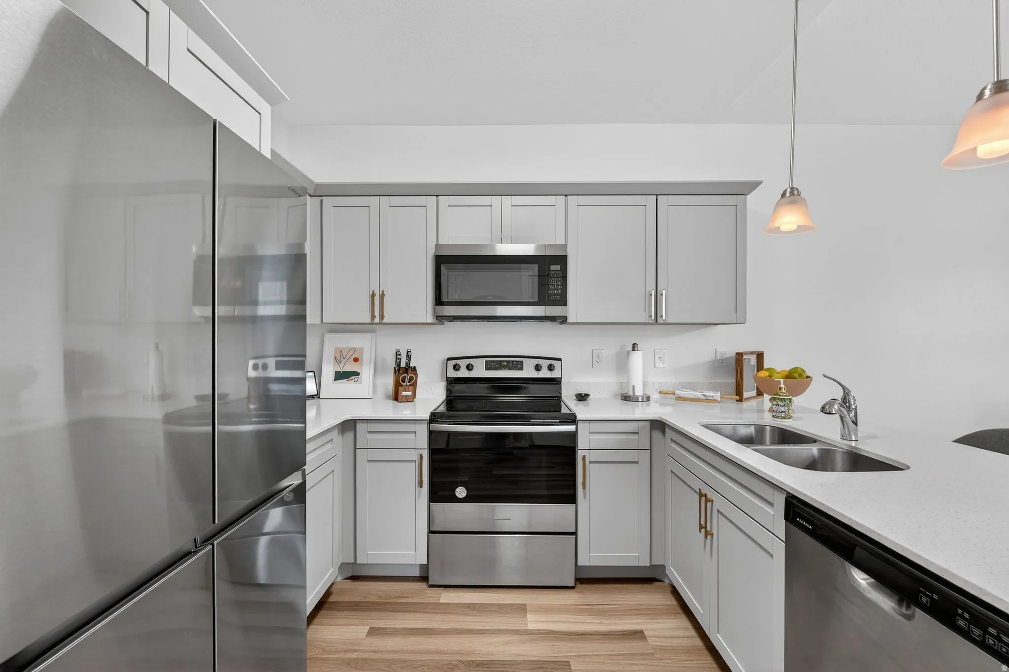 Kitchen featuring stainless steel appliances, gray cabinets, light stone counters, and hanging light fixtures
