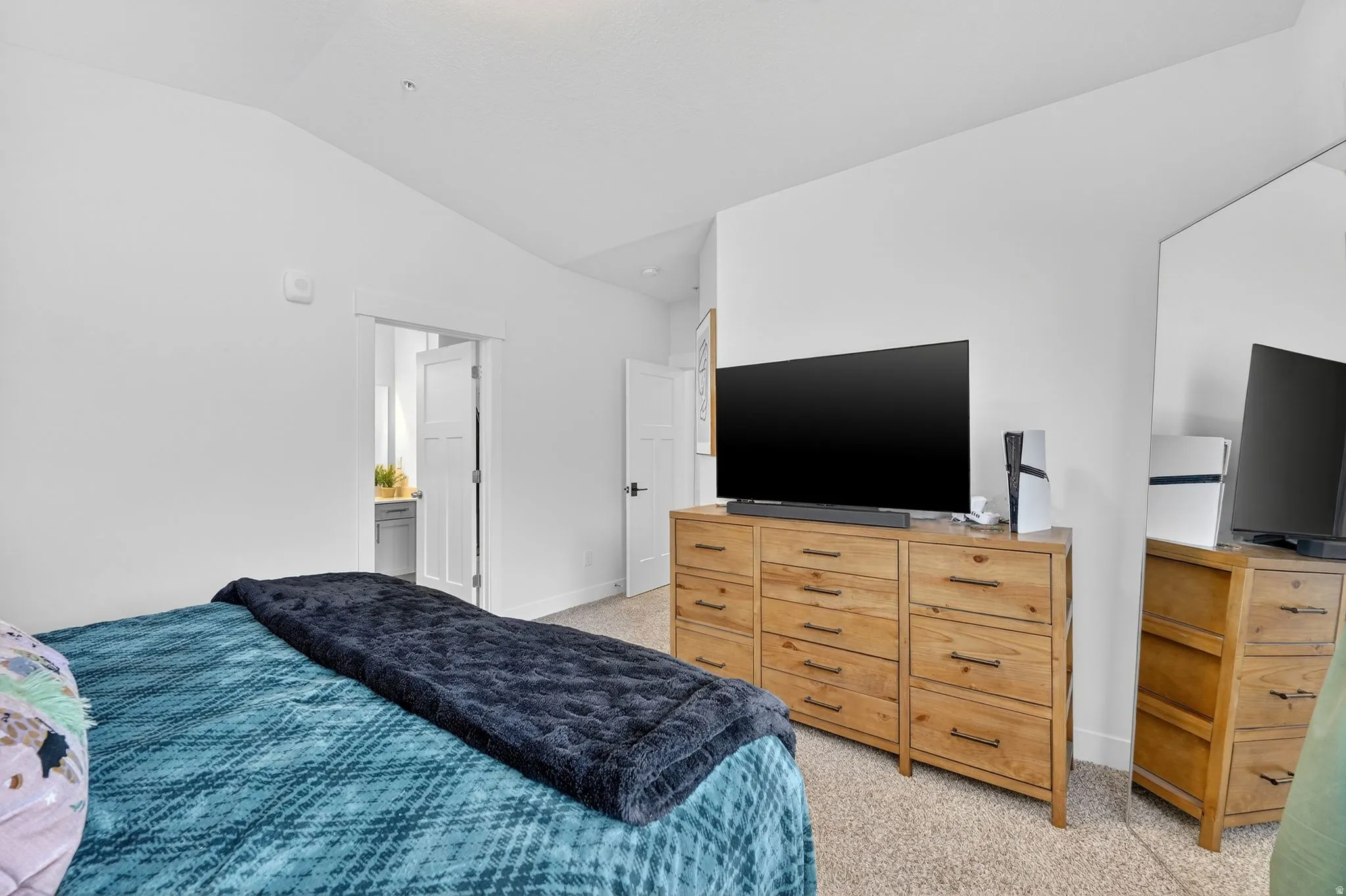 Bedroom featuring light carpet, lofted ceiling, and ensuite bath