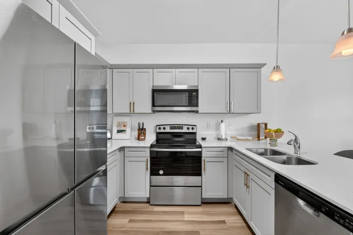 Kitchen featuring stainless steel appliances, gray cabinets, light stone counters, and hanging light fixtures