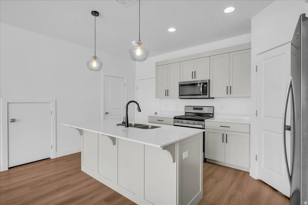 Kitchen featuring light wood-type flooring, stainless steel appliances, a kitchen bar, a kitchen island with sink, and decorative light fixtures