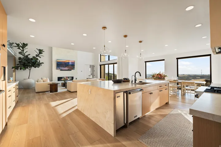 Kitchen with light wood finish cabinets, open floor plan, a center island with sink, a fireplace, and light wood-style floors
