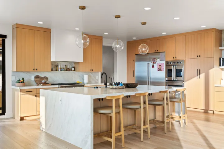 Kitchen featuring stainless steel appliances, light wood finish cabinets, light stone counters, and light wood finished floors