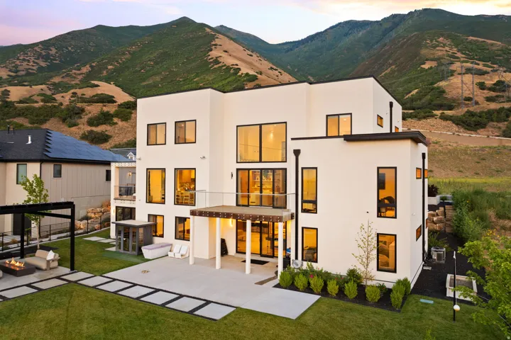 Back of house at dusk featuring a lawn, a mountain view, a patio, and stucco siding