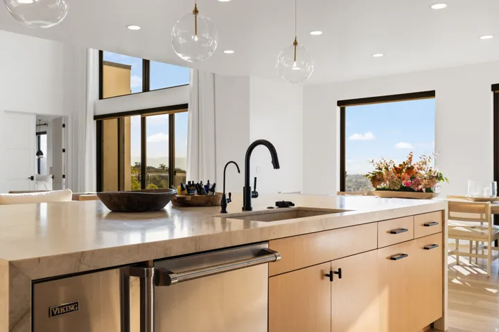 Kitchen with stainless steel dishwasher, light stone countertops, hanging light fixtures, light wood finish cabinetry, and light wood-style flooring