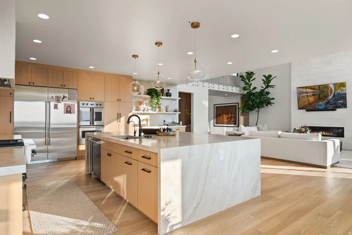 Kitchen featuring a large fireplace, light wood finish cabinets, a center island with sink, and stainless steel appliances