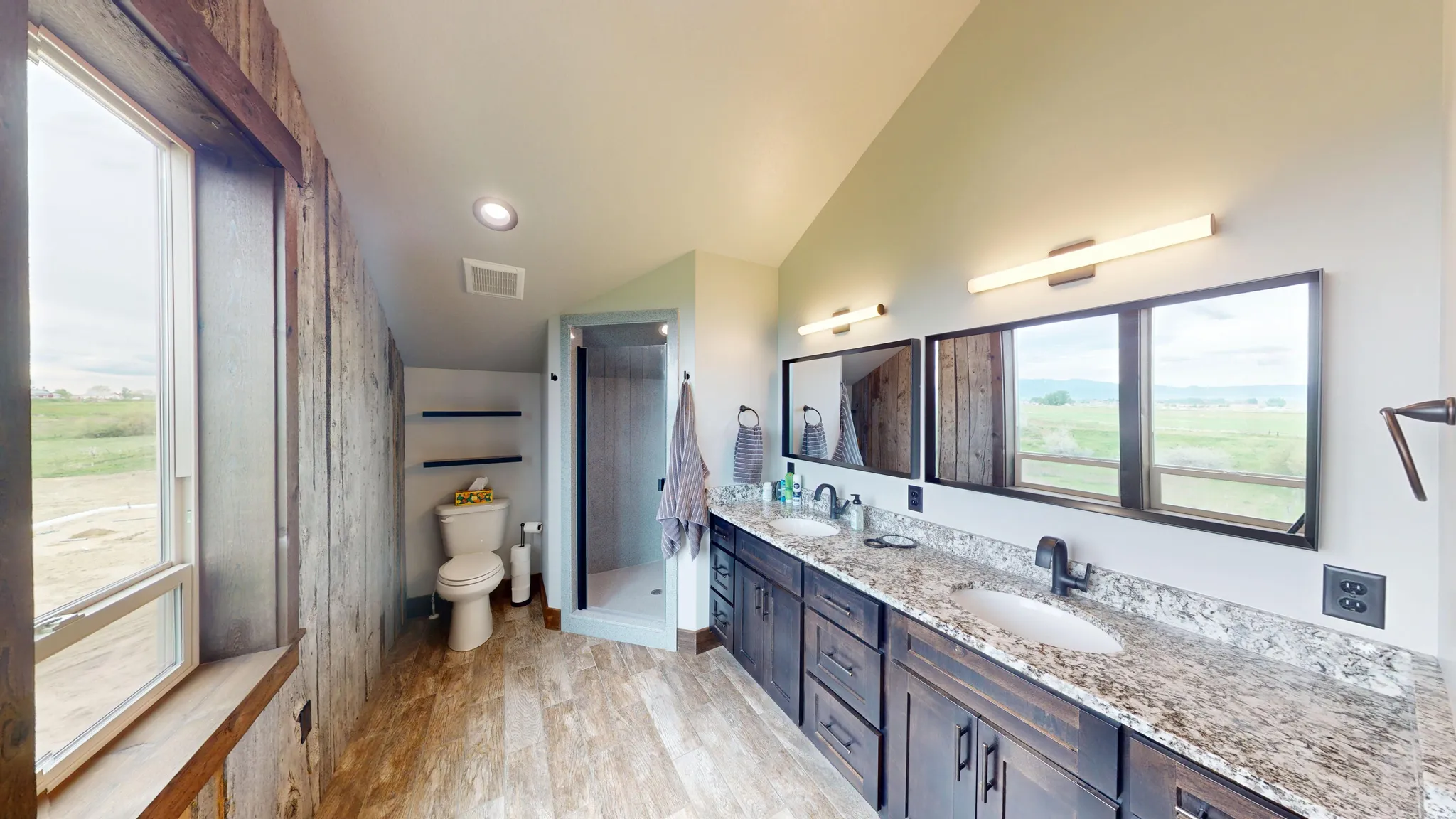 Full bath with double vanity, a shower stall, lofted ceiling, and light wood finished floors