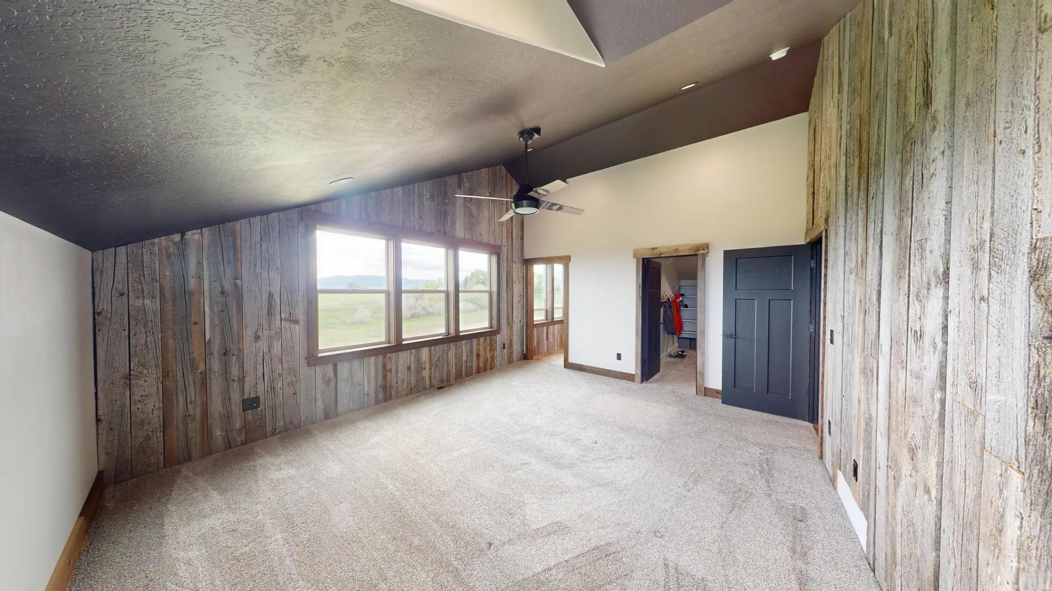 Unfurnished bedroom with wooden walls, a walk in closet, a high textured ceiling, light carpet, and an accent wall